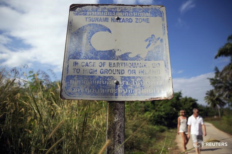 © Reuters. Туристы у знака, предупреждающего об опасности цунами, в городе Као Лак в Таиланде