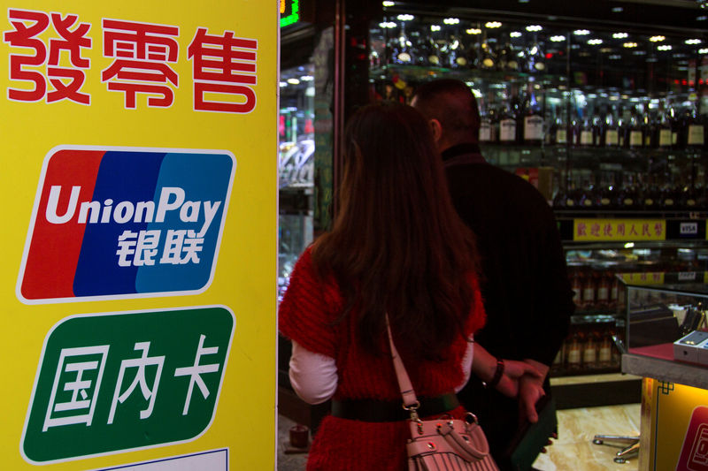 © Reuters. Chinese visitors walk past a sign for China UnionPay outside a pawnshop in Macau