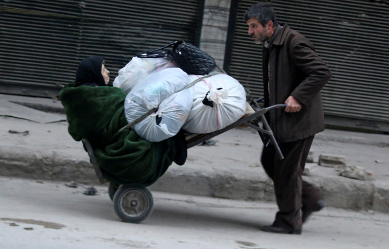 © Reuters. A man pushes a cart carrying an elderly woman and belongings as they flee deeper into the remaining rebel-held areas of Aleppo