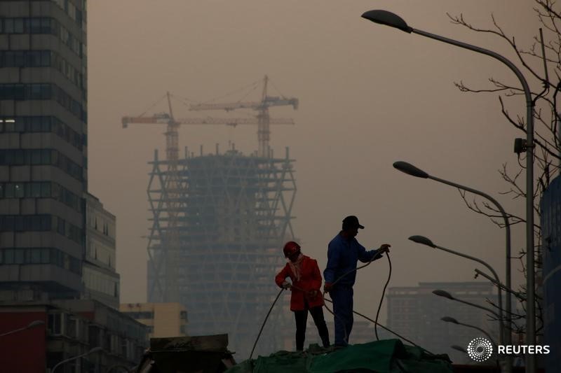 © Reuters. Workers strap a tarpaulin across the top of a truck outside a construction site in Beijing