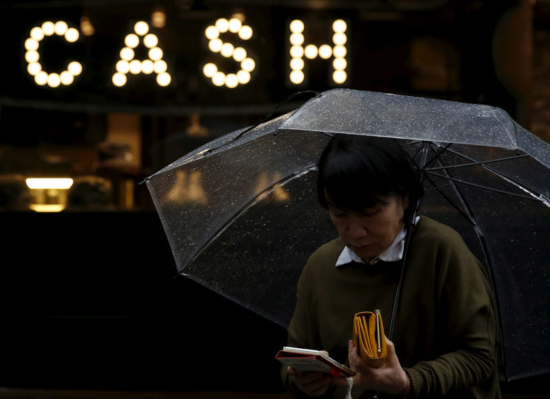 © Reuters. A pedestrian holding an umbrella and her wallet walks past the word "CASH" part of a sign on a street at a shopping district in Tokyo