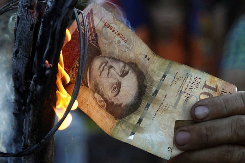 © Reuters. A man burns a 100-bolivar bill during a protest in El Pinal