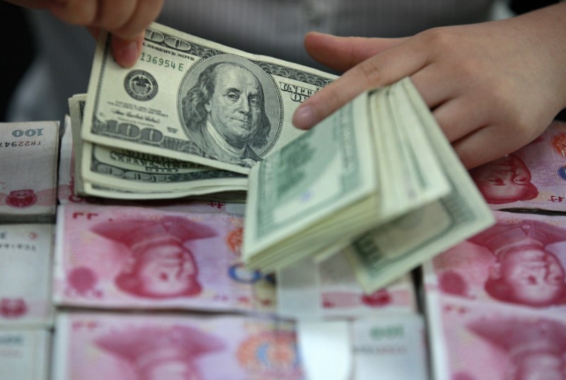 © Reuters. A bank clerk counts U.S. dollar banknotes on bundles of 100 Chinese yuan banknotes at a branch of a bank in Huaibei