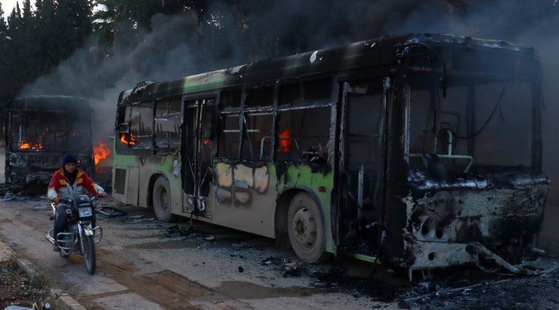 © Reuters. A man on a motorcycle drives past burning buses while en route to evacuate ill and injured people from the besieged Syrian villages of al-Foua and Kefraya, after they were attacked and burned, in Idlib province