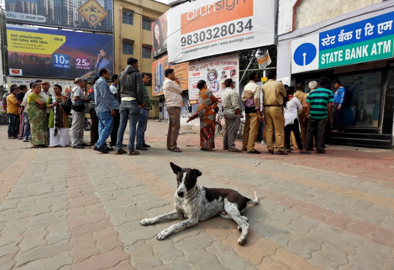 © Reuters. A stray dog rests as people queue outside an ATM to withdraw cash in Kolkata