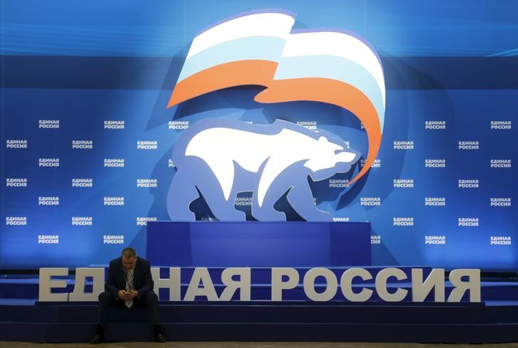 © Reuters. Мужчина с мобильным телефоном сидит у логотипа партии "Единая Россия" на партийном съезде в Москве