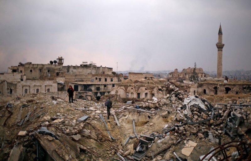 © Reuters. A member of forces loyal to Syria's President Bashar al-Assad stands with a civilian on the rubble of the Carlton Hotel, in the government controlled area of Aleppo