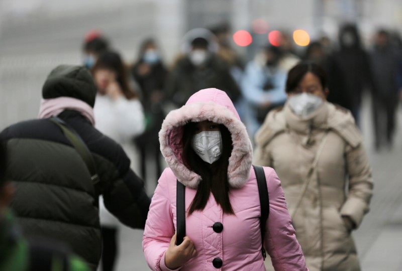 © Reuters. People wearing masks walk toward an office building during the smog in Beijing