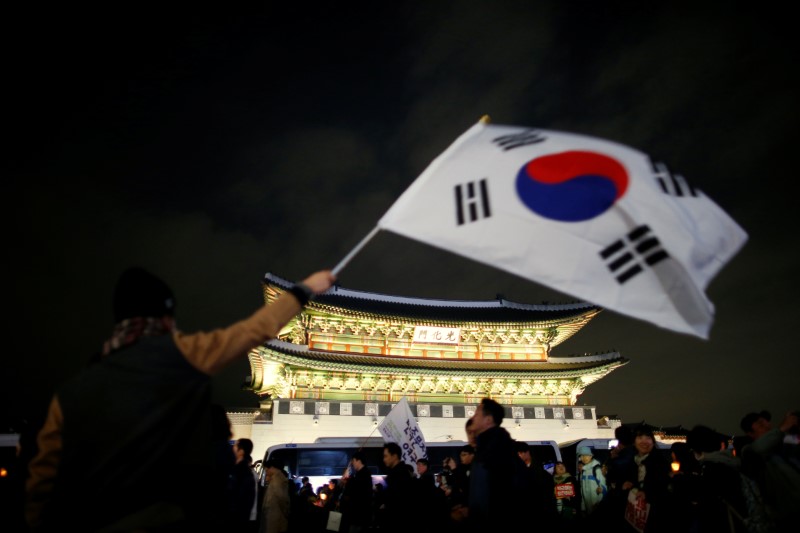 © Reuters. A man waves a national flag as people march toward the Presidential Blue House during a rally demanding President Park Geun-hye to step down in central Seoul