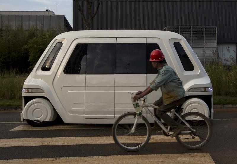 © Reuters. A worker rides a bike past a driverless vehicle at Vanke's Building Research Centre testing area in Dongguan