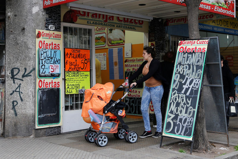 © Reuters. A woman pushing a baby carriage walks past a shop selling farm products in Buenos Aires