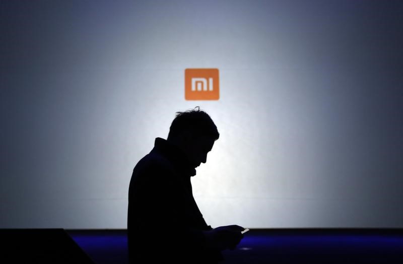 © Reuters. A man uses his mobile phone in front of a screen showing a logo of Xiaomi in Beijing