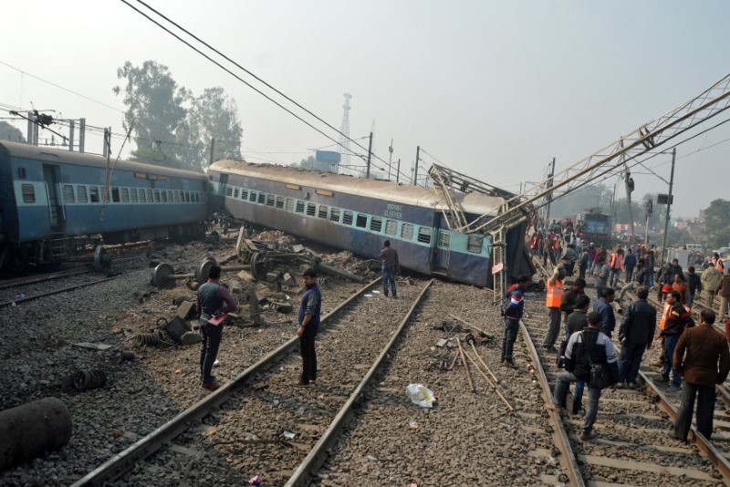 © Reuters. Rescuers and railway officials stand next to damaged coaches of a passenger train after it derailed near Kanpur