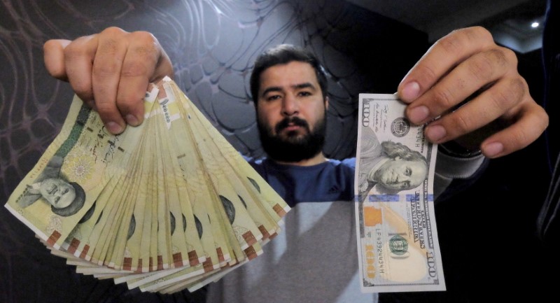 © Reuters. Money changer poses for the camera with U.S hundred dollar bill and the amount being given when converting it into Iranian rials, at a currency exchange shop in Tehran's business district, Iran