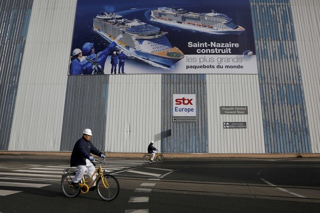 © Reuters. FILE PHOTO Shipbuilders ride past a giant poster at the STX Les Chantiers de l'Atlantique shipyard site in Saint-Nazaire