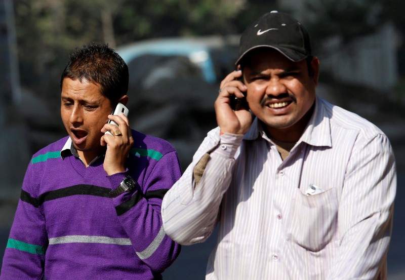 © Reuters. Men talk on their mobile phones while walking on a road in Kolkata