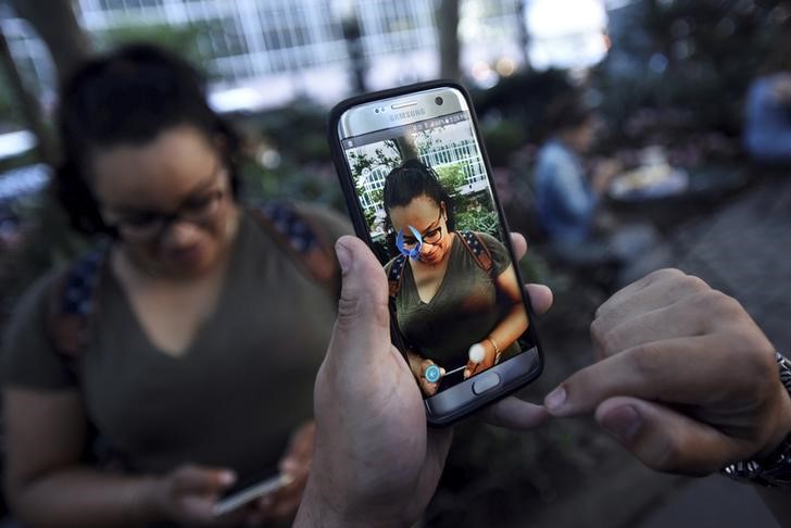 © Reuters. A Pokemon appears on the screen next to a woman as a man plays the augmented reality mobile game "Pokemon Go" by Nintendo in Bryant Park in New York City