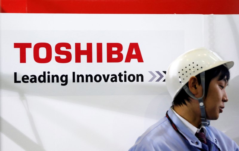 © Reuters. An employee stands next to a logo of Toshiba Corp during a demonstration of the company's new four-legged robot, at the company's Yokohama complex in Yokohama, south of Tokyo