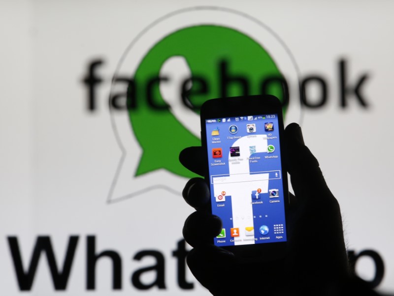 © Reuters. An illustration photo shows a man holding a smart phone with a Facebook logo as its screen wallpaper in front of a WhatsApp messenger logo, in Zenica