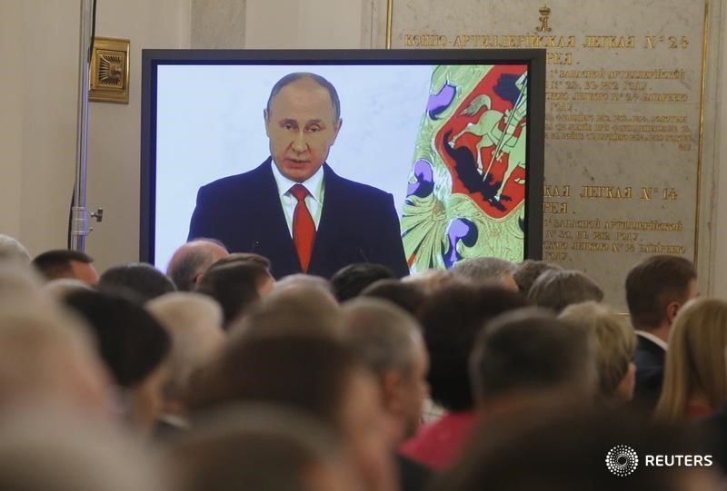 © Reuters. Люди слушают ежегодное обращение Владимира Путина к нации