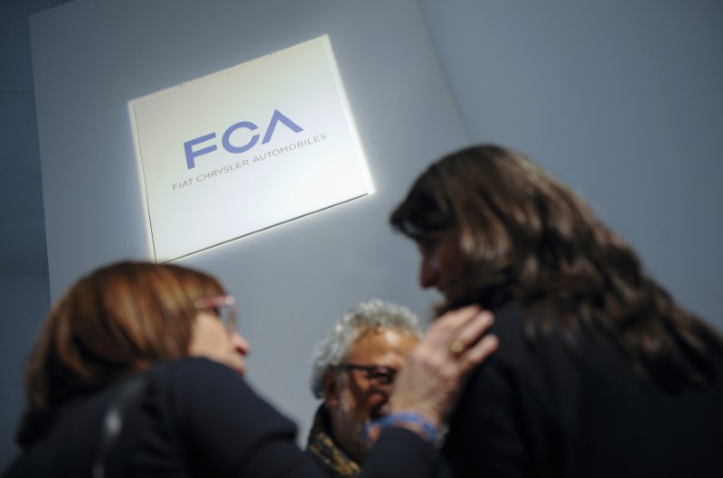 © Reuters. People talk as they stand next to a logo of Fiat Chrysler Automobiles (FCA) in Turin