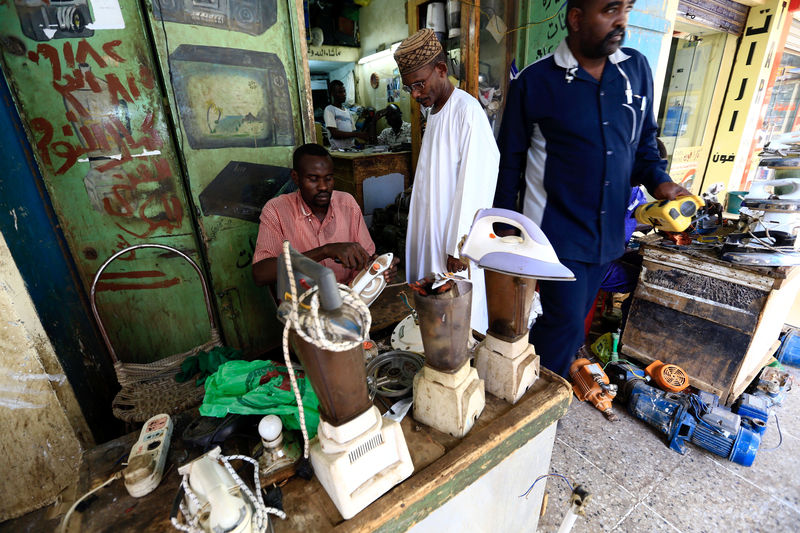 © Reuters. A man waits as a worker repairs an iron at a market in Khartoum