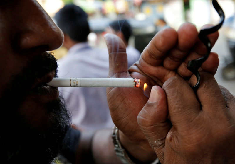 © Reuters. FILE PHOTO -  A man lights a cigarette along a road in Mumbai