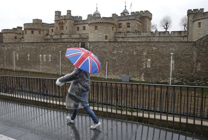 © Reuters. A tourist carrying a Union Flag umbrella walks in the rain during a spell of wet weather next to The Tower of London, in London