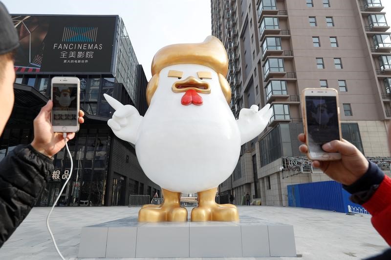 © Reuters. People take pictures with mobile phones of a sculpture of a rooster that local media say bears resemblance to U.S. President-elect Donald Trump, outside a shopping mall in Taiyuan