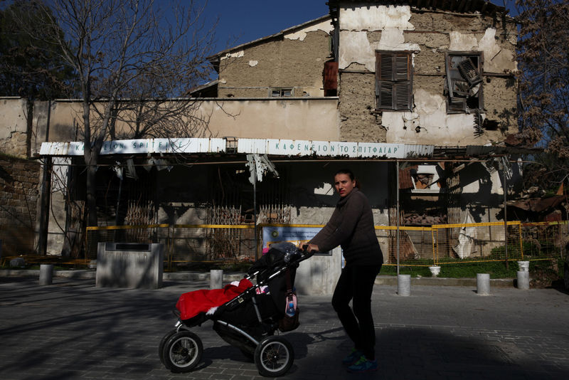 © Reuters. An woman pushes a baby stroller in front of an abandoned building, in the UN-controlled buffer zone in Nicosia