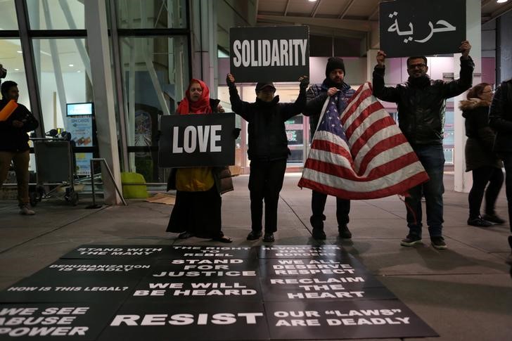 © Reuters. Protesters hold signs in opposition to U.S. President Donald Trump's ban on immigration and travel outside Terminal 4 at JFK airport in Queens
