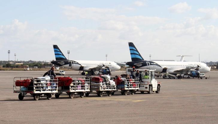 © Reuters. Workers transport luggages near Afriqiyah Airways planes parked at Tripoli International Airport in Libya