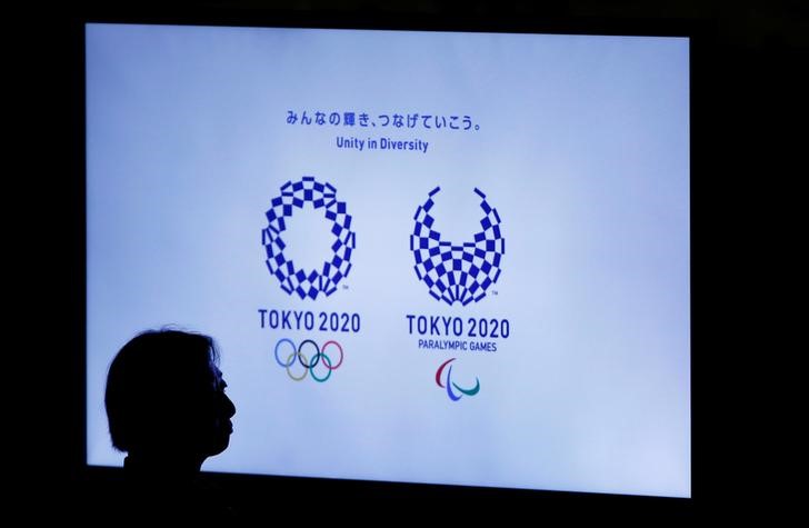 © Reuters. A woman is silhouetted against a monitor showing Tokyo 2020 Olympics and Paralympics emblems during the Olympic and Paralympic flag-raising ceremony at Tokyo Metropolitan Government Building in Tokyo