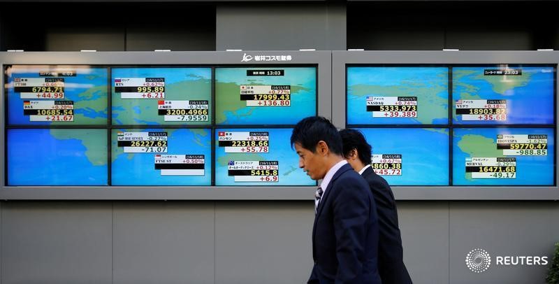© Reuters. Tokyo, passanti davanti ai tabelloni elettronici di un brokerage