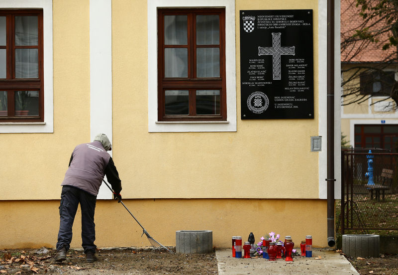 © Reuters. A man cleans a street next to a plaque containing a pro-nazi salute honoring Croatian fighters killed during the 1990s' war in Jasenovac