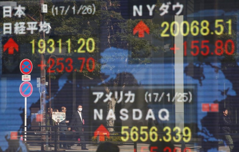 © Reuters. Pedestrians are reflected on an electronic board showing Japan's Nikkei average, the Dow Jones average and the stock averages of other countries outside a brokerage in Tokyo