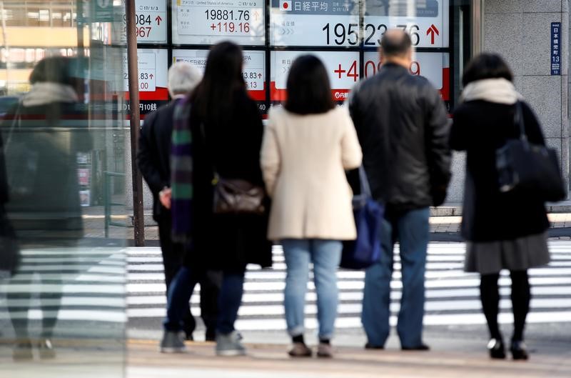 © Reuters. People are seen in front of an electronic board showing stock prices outside a brokerage at a business district in Tokyo