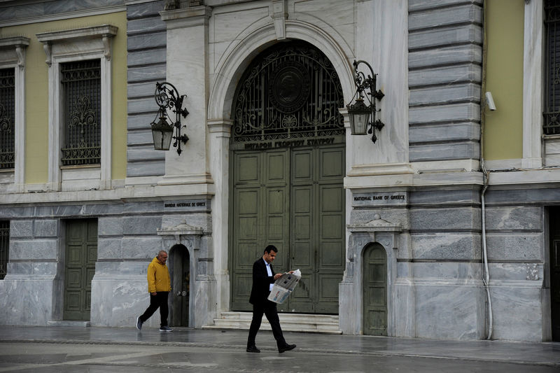 © Reuters. A man reads his newspaper as he walks past the National Bank of Greece headquarters in central Athens