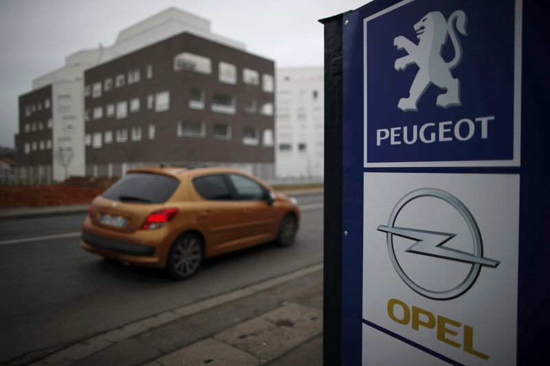 © Reuters. A Peugeot car drives past the logos of French car maker Peugeot and German car maker Opel at a dealership in Villepinte