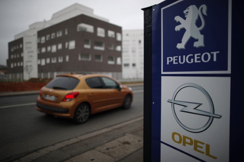 © Reuters. A Peugeot car drives past the logos of French car maker Peugeot and German car maker Opel at a dealership in Villepinte