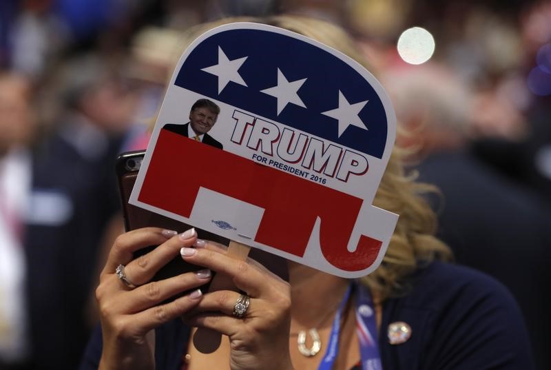 © Reuters. A delegate takes a photograph with her phone as she holds a small sign supporting Republican U.S. presidential nominee Trump during the final day of the Republican National Convention in Cleveland