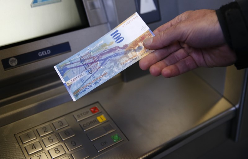 © Reuters. A man holds a 100 Swiss Francs bank note in front of an ATM in this illustration picture taken in Bern