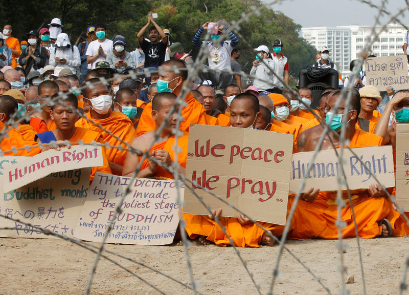 © Reuters. Buddhist monks pray and hold placards behind a wire barricade at Dhammakaya temple