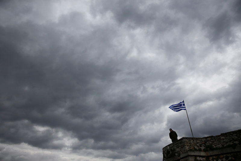 © Reuters. A man looks down as a Greek national flag flutters atop one of the bastions of the 17th century fortress of Palamidi under an overcast sky at the southern port city of Nafplio