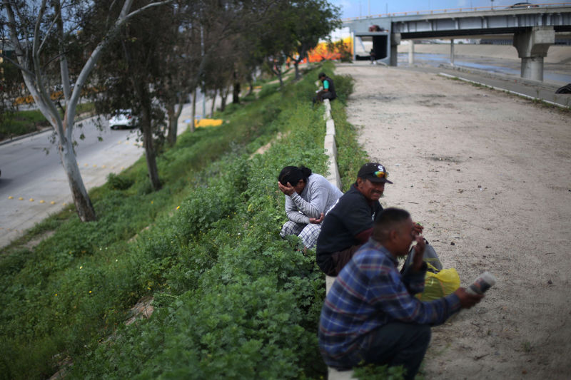 © Reuters. A Mexican who was recently deported from the U.S. gestures next to others sitting by the Tijuana river, in Tijuana