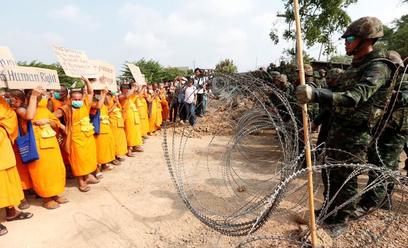© Reuters. Buddhist monks stand in front of soldiers between a wire barricade Dhammakaya temple, as they leave to receive food from the people in Pathum Thani province
