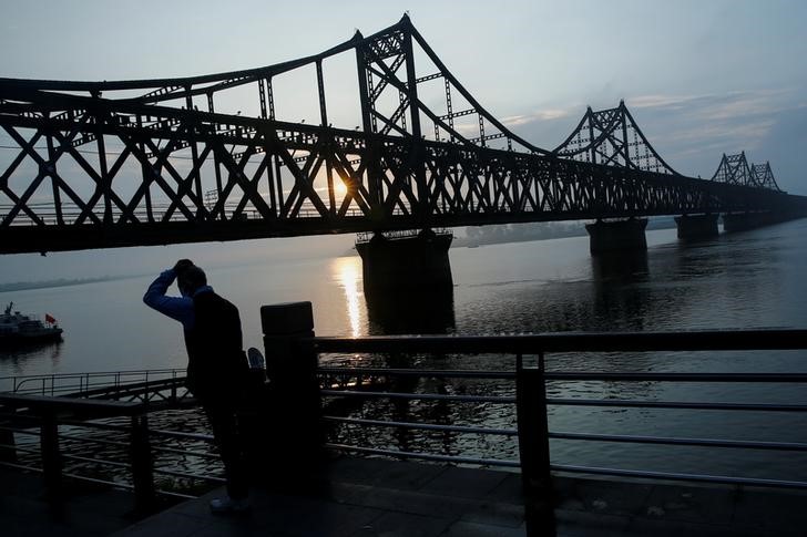 © Reuters. A man watches the sun rise behind the bridge over Yalu River that connects China's Dandong, Liaoning province, and North Korea's Sinuiju
