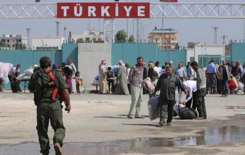 © Reuters. Kurdish People's Protection Units fighter walks near residents who had fled Tel Abyad as they re-enter Syria from Turkey, after the YPG took control of the area in Tel Abyad town, Raqqa governorate, Syria