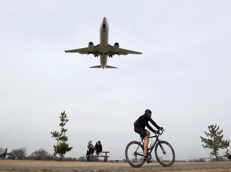 © Reuters. A plane prepares to land over a cyclist during unseasonably warm weather at Reagan National Airport in Washington