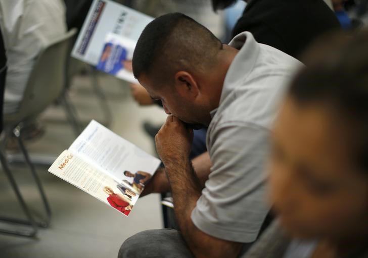 © Reuters. People read pamphlets as they wait in line at a health insurance enrollment event in Cudahy